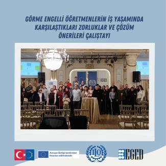 Görselde ortada büyük bir grup insan var; otel veya konferans salonunda toplanmışlar. Üstte koyu mavi yazıyla "GÖRME ENGELLİ ÖĞRETMENLERİN İŞ YAŞAMINDA KARŞILAŞTIKLARI ZORLUKLAR VE ÇÖZÜM ÖNERİLERİ ÇALIŞTAYI" yazısı yer alıyor. Grup fotoğrafının ön planında boş sıralar ve ortada yüksek bir yuvarlak masa üzerinde örtü var. Arka planda büyük bir avize, sahne ışıkları ve duvarda çeşitli pankartlar/gösterimler bulunuyor.