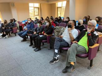 Toplantı salonunda bir atölye çalışmasında masanın iki tarafında Oğuzhan ve kadın-erkek katılımcılar bir şeyler konuşurken görülüyor.