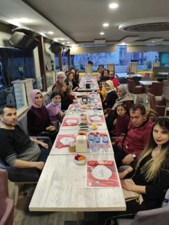 Farklı Açılardan, masaların iki ayrı ucundan, çekilen fotoğraflarda, dikdörtgen iki uzun masada kadın erkek katılımcılar karşılıklı ve yan yana otururken ve gülümserken görülmekteler.