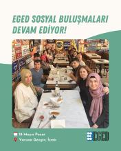 Bir kafede uzun bir masanın etrafında oturan yaklaşık on iki kişilik bir grup. Masada çay bardakları, tabaklar, zeytin ve ekmek gibi kahvaltılıklar var. İnsanlar birbirine yakın oturmuş, çoğu kameraya bakıyor ve gülümsüyor. Arka planda duvarlarda çeşitli tabelalar ve dekoratif objeler asılı. Fotoğrafın üst kısmında büyük harflerle “EGED SOSYAL BULUŞMALARI DEVAM EDİYOR!” yazıyor. Alt kısımda ise 18 Mayıs Pazar günü, Varuna Gezgin, İzmir’de buluşmanın gerçekleştiği belirtilmiş.
