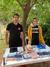 Fotoğrafta Şeyma ve Hasan stant arkasında poz veriyor. Sergilenen eşyalar ve etrafın yeşilliği de kadraja girmiş.